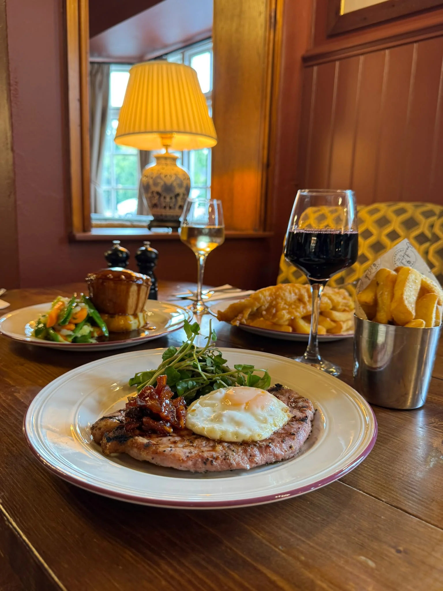 Grilled gammon topped with a fried egg, served with chips and greens