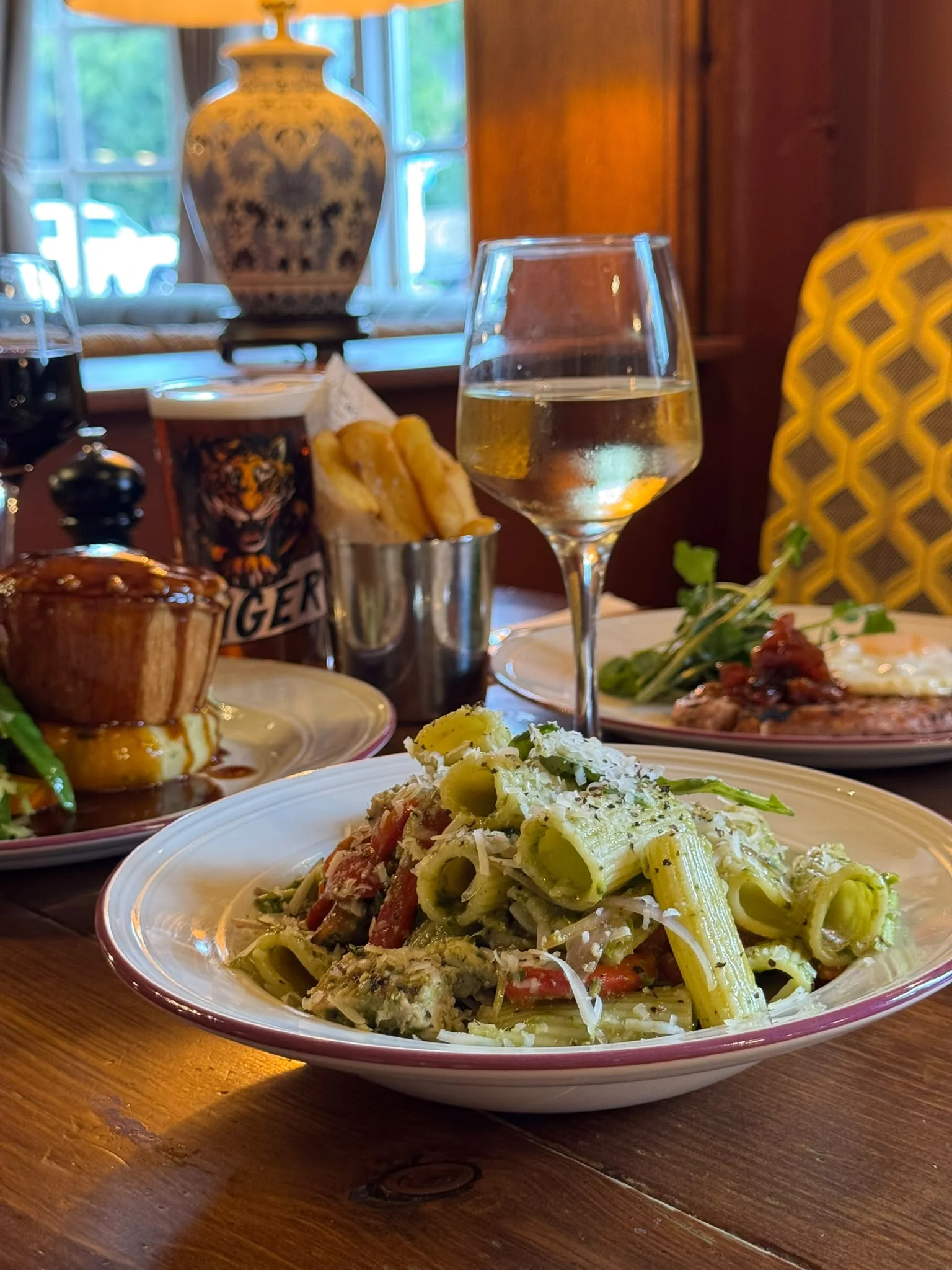 A bowl of pasta with vegetables and grated cheese beside a glass of white wine