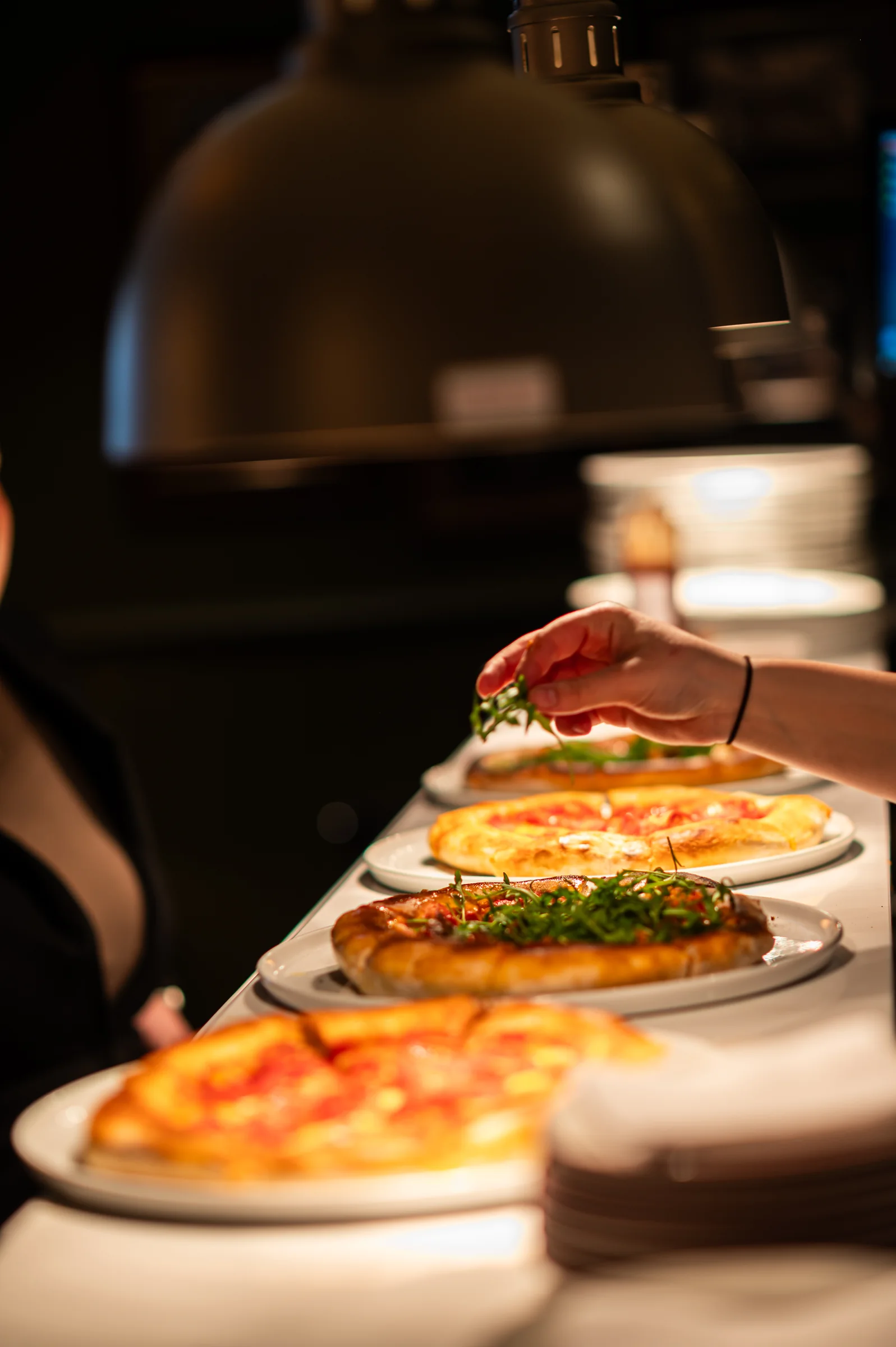 Freshly prepared pizzas beneath a kitchen heat lamp