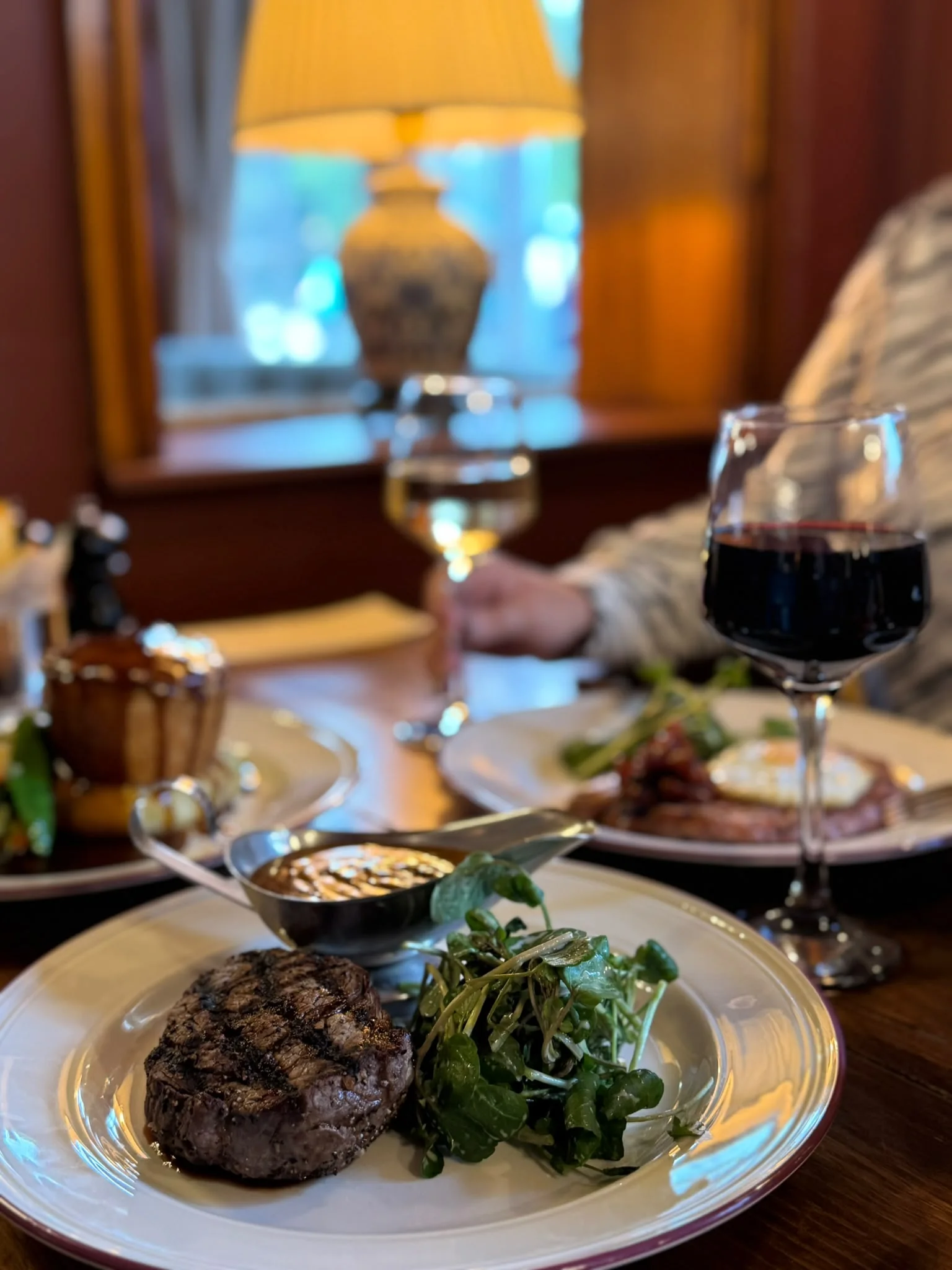 Steak served with greens and sauce beside a glass of red wine