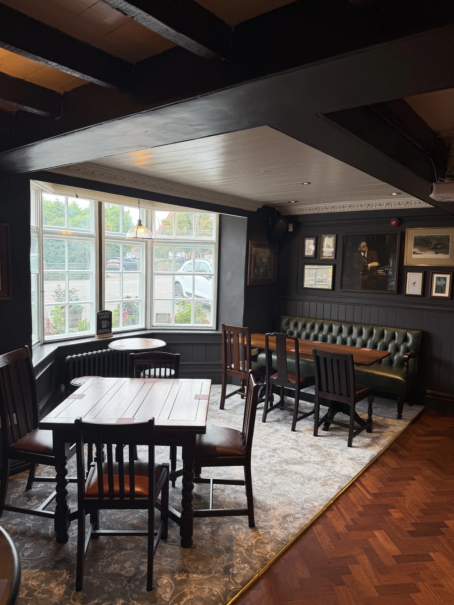 Wooden tables and upholstered seating beside the pub windows